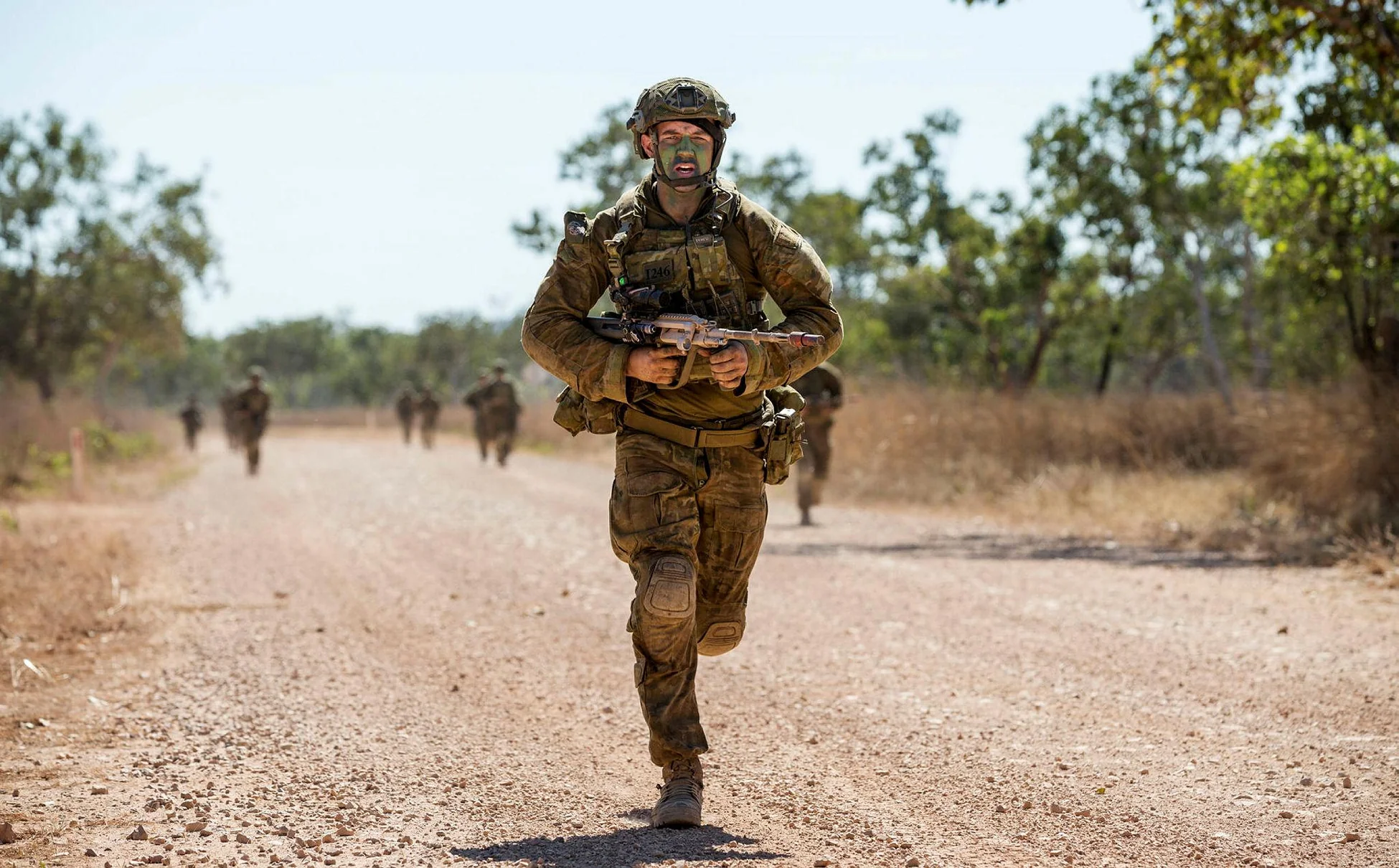 Soldier in full combat gear performing a tactical run across arid desert terrain